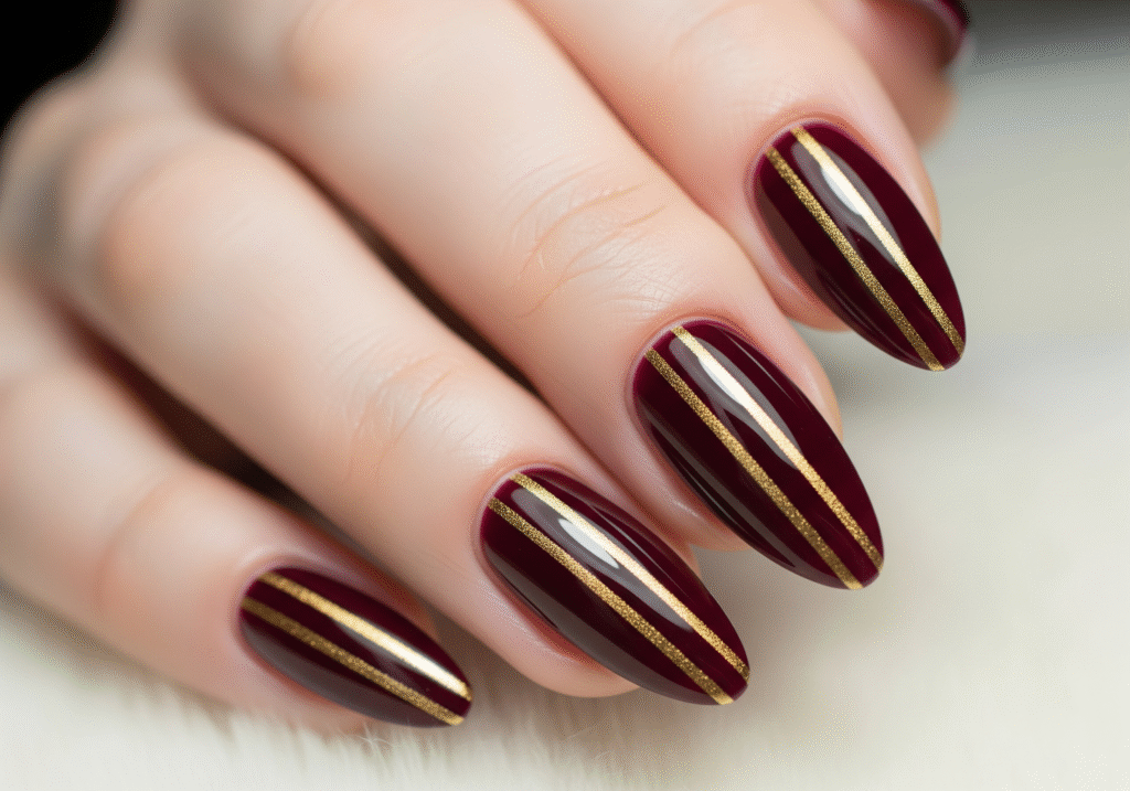 Deep burgundy nails with thin gold striping.